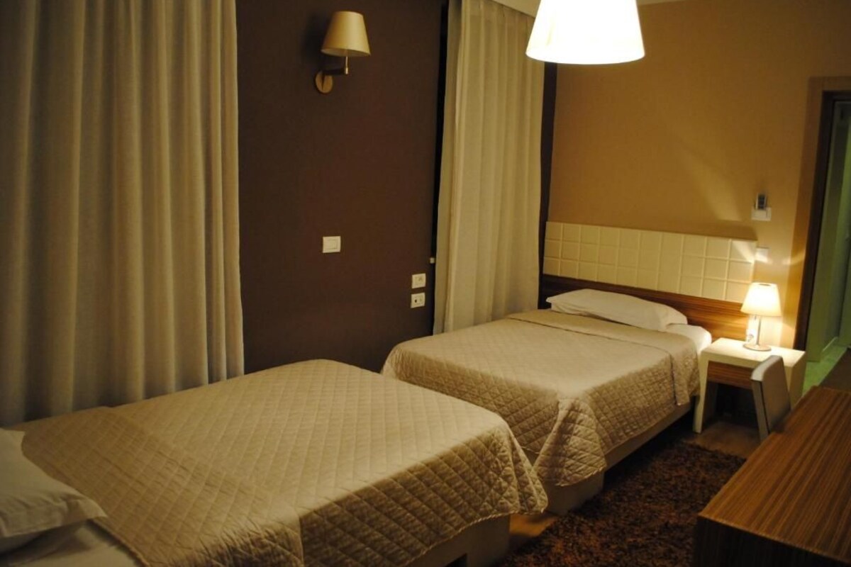 Quarto de hotel com duas camas, uma mesa de cabeceira, um abajur e um espelho.