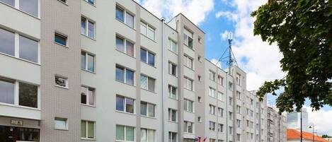 Un edificio residencial de varios pisos con fachada uniforme, varias ventanas y una bandera visible.