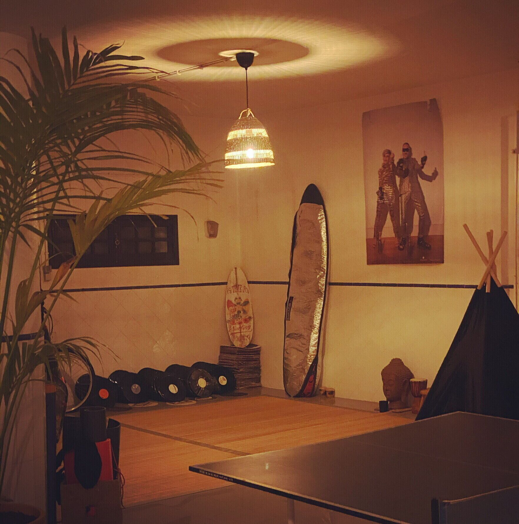 A room with a ceiling fan, a surfboard, a poster, and a plant.