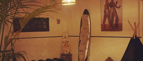 A room with a ceiling fan, a surfboard, a poster, and a plant.