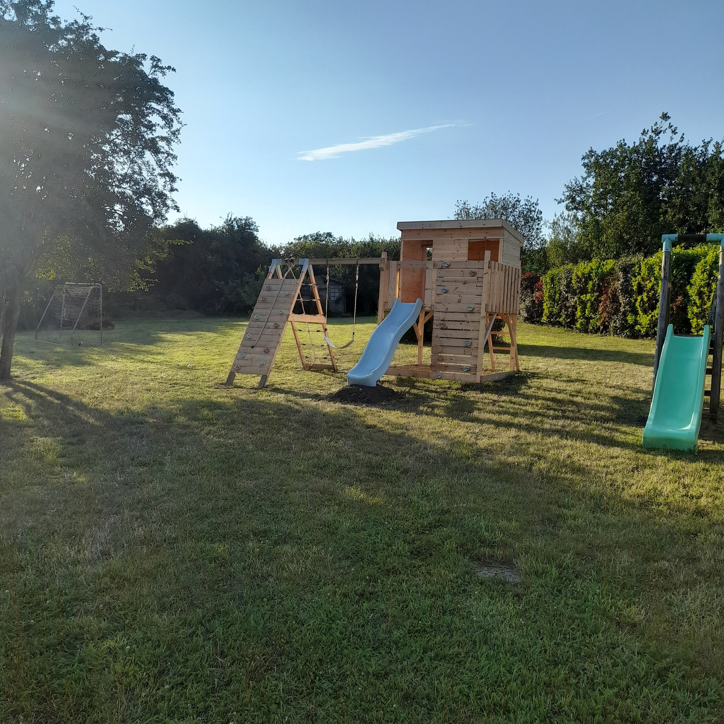 A playground with a slide, climbing wall, and a wooden playhouse.