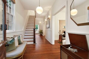 Un couloir doté d’un plancher en bois, d’un escalier, d’un banc avec des coussins et d’un éclairage suspendu.