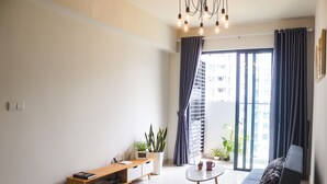 A modern living room with a sofa, a coffee table, a bookshelf, and a potted plant. - Spacious and Modern Service Apartment in Hochiminh (Ho Chi Minh City)