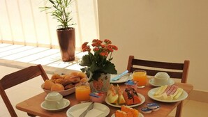 A wooden dining table with plates of food, a bowl of bread, a potted plant, and a vase of flowers. - Pousada Recanto das Vertentes (Capitólio)