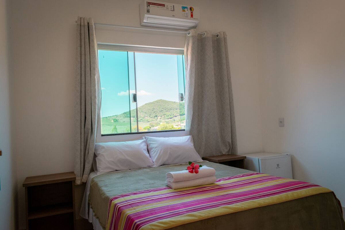 Une chambre d’hôtel avec un lit, une fenêtre avec des rideaux, une petite table et un climatiseur fixé au mur.