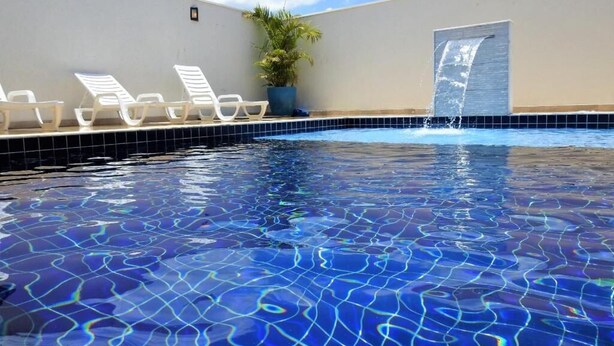 A swimming pool with clear blue water, white lounge chairs, and a potted plant. - Pousada Recanto das Vertentes (Capitólio)