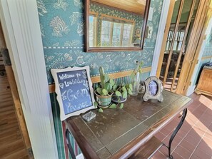 A chalkboard sign with 'Welcome to LearniVille's Green Place' written on it, a potted plant, a small mirror, and a window with a view of greenery.