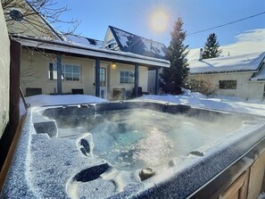 A hot tub in a snowy outdoor setting with a house in the background.