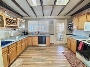 A modern kitchen with wooden cabinets, a dishwasher, a stove, and a window with blinds.