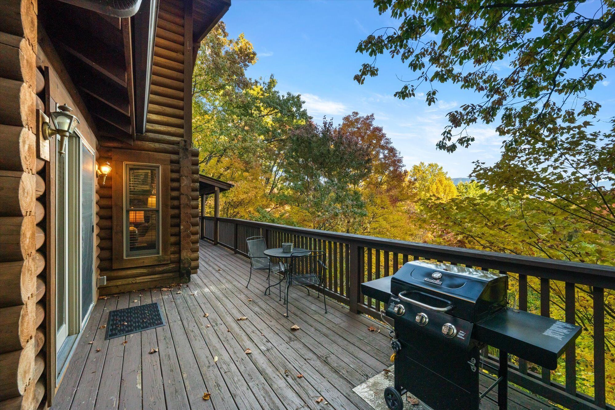 Eine Holzterrasse mit Grill und Sitzgelegenheit, mit Blick auf ein bewaldetes Gebiet.