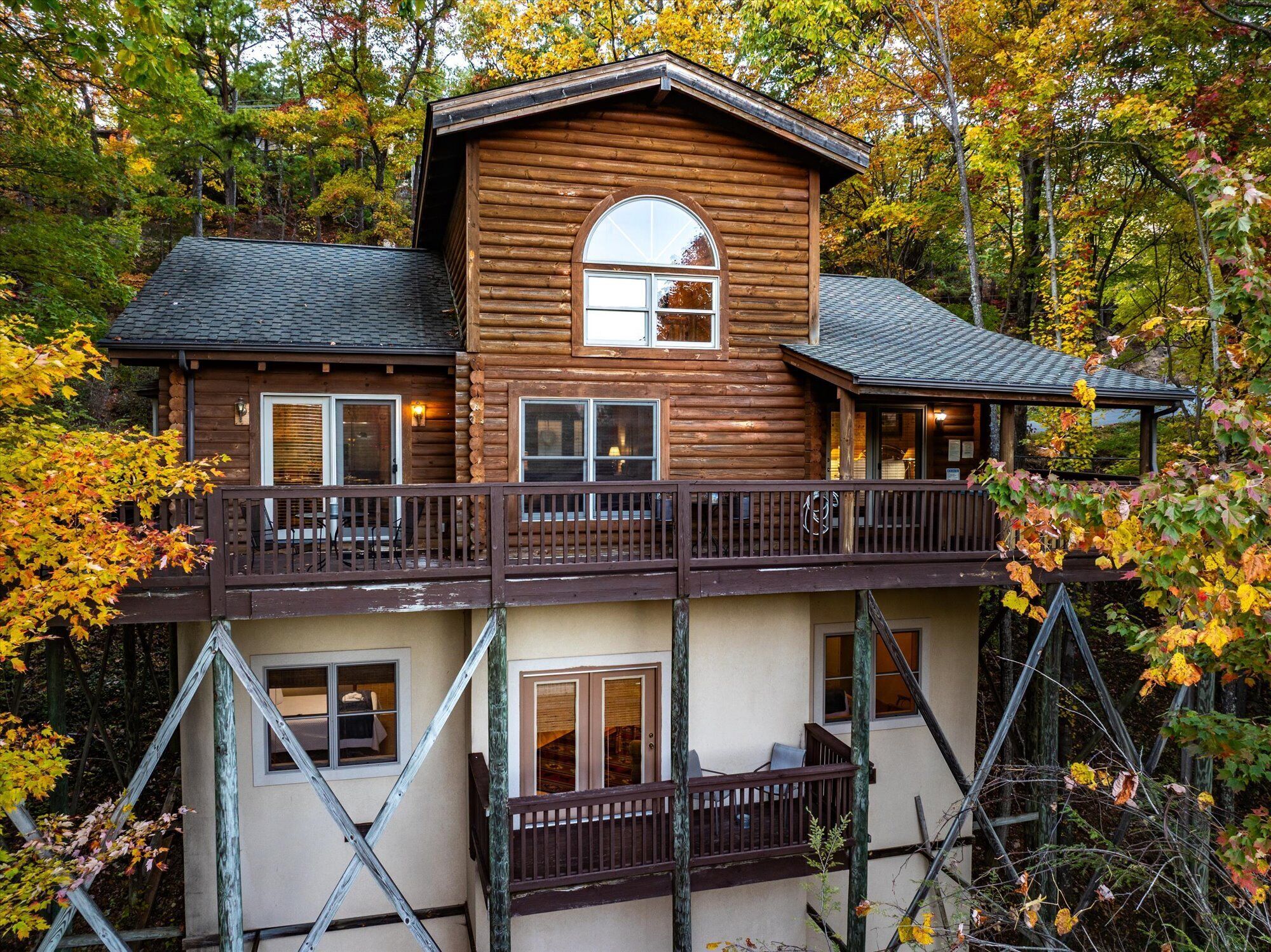 A two-story log cabin with a balcony, surrounded by autumn foliage.