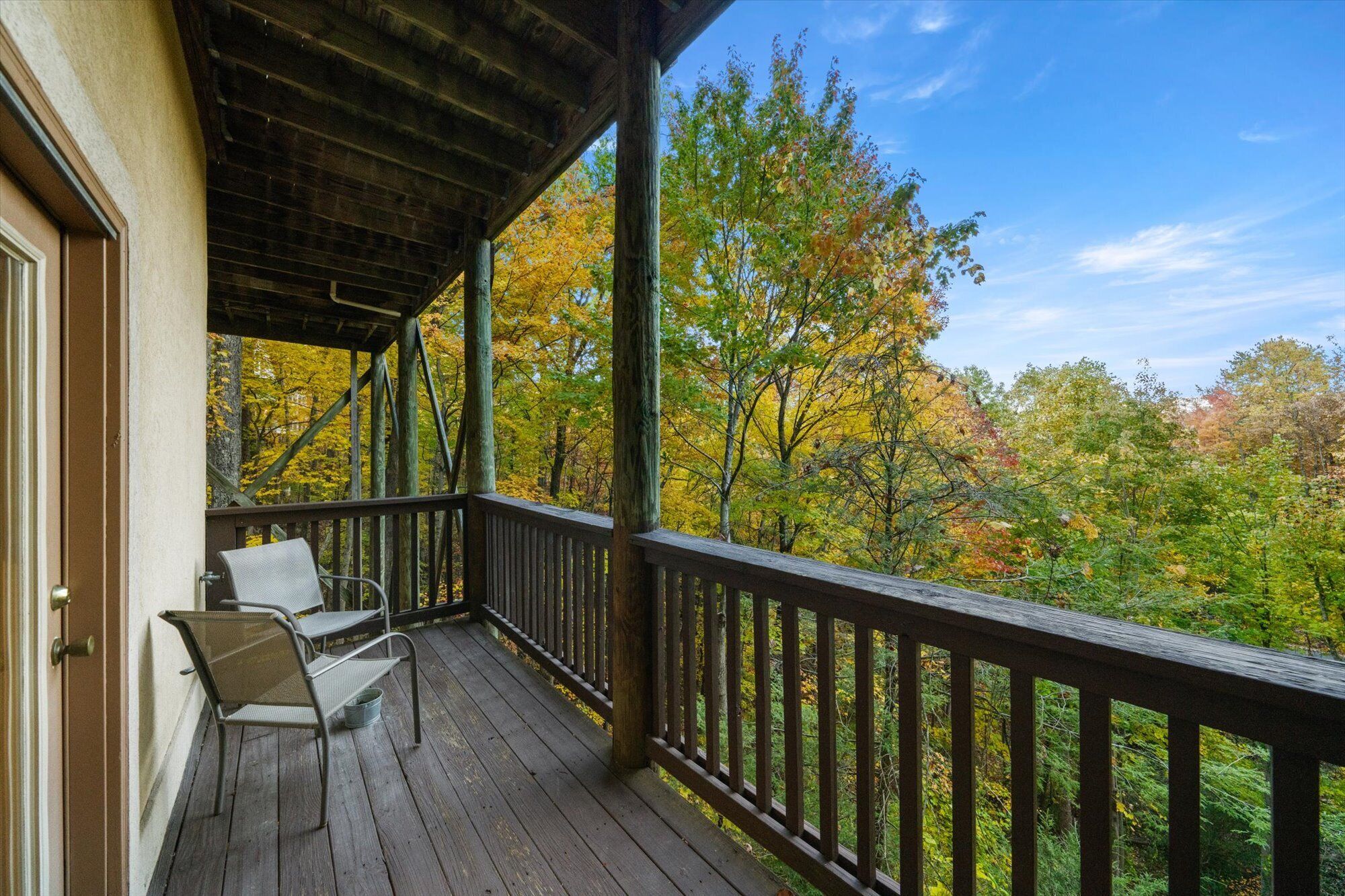 A wooden deck with a railing, two chairs, and a view of autumn foliage.