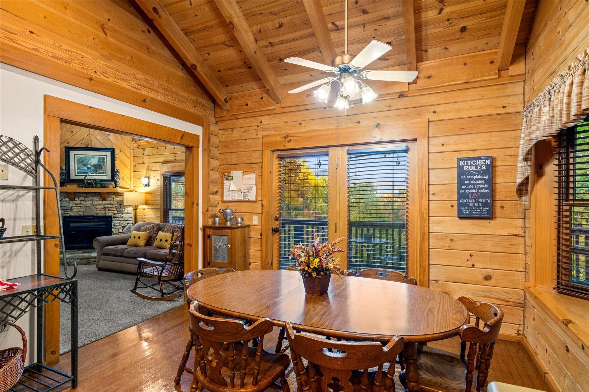 A cozy cabin interior with a wooden dining table, chairs, a fireplace, and a ceiling fan.