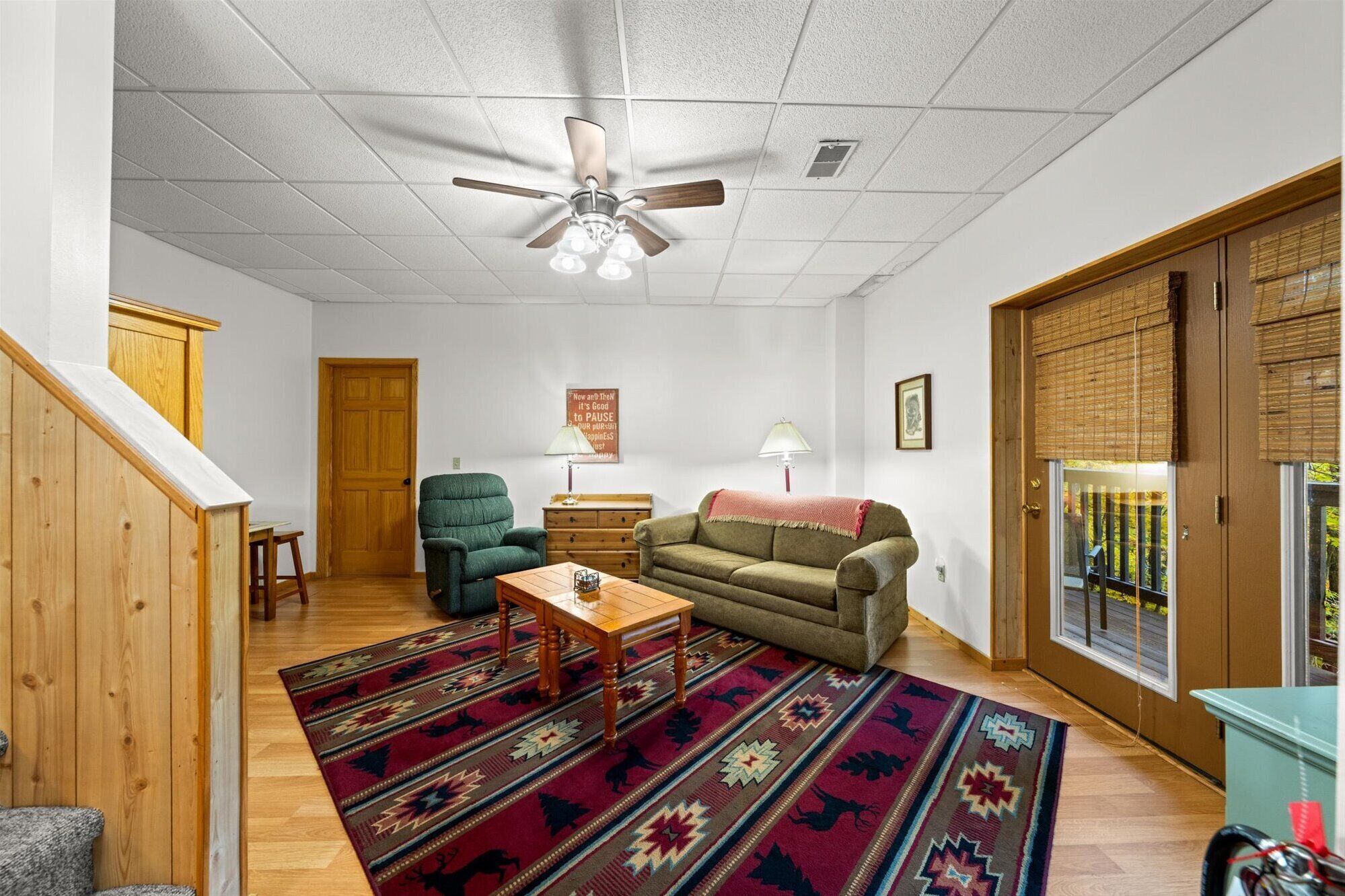 A living room with a ceiling fan, a green armchair, a sofa, a patterned rug, and a wooden staircase.