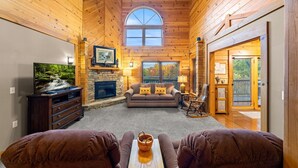 Ein gemütliches Blockhaus-Interieur mit Kamin aus Stein, einem Fernseher und einer bequemen Sitzecke.