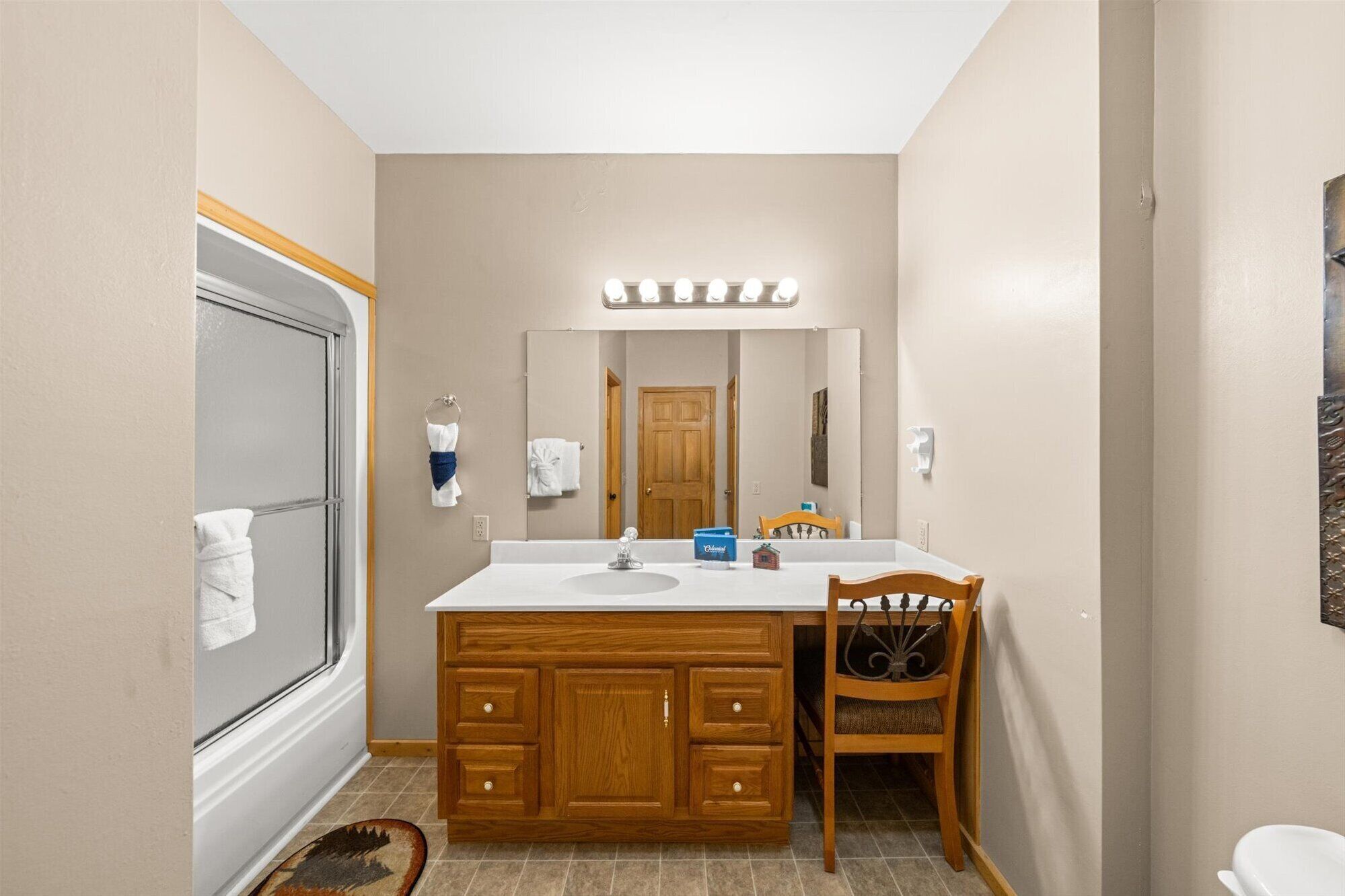 A bathroom with a vanity, a mirror, and a chair.