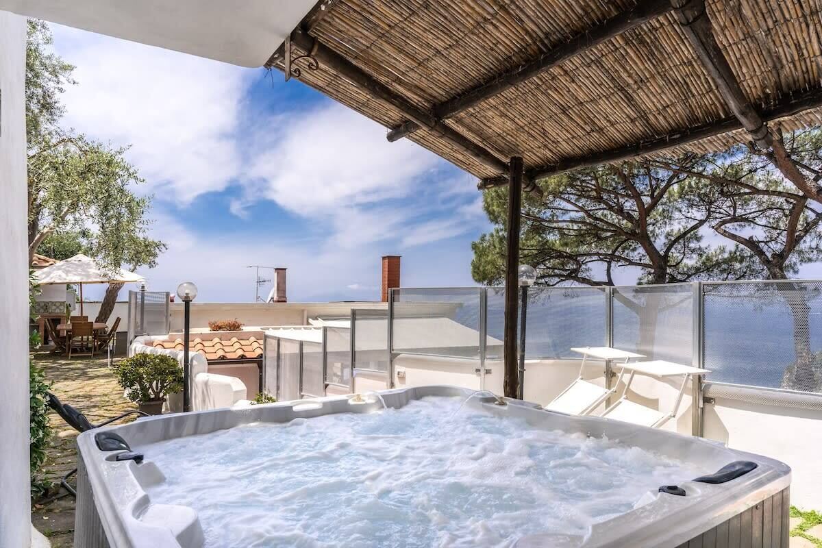 Un espace avec jacuzzi offrant une vue sur la mer, des sièges extérieurs et un patio couvert.