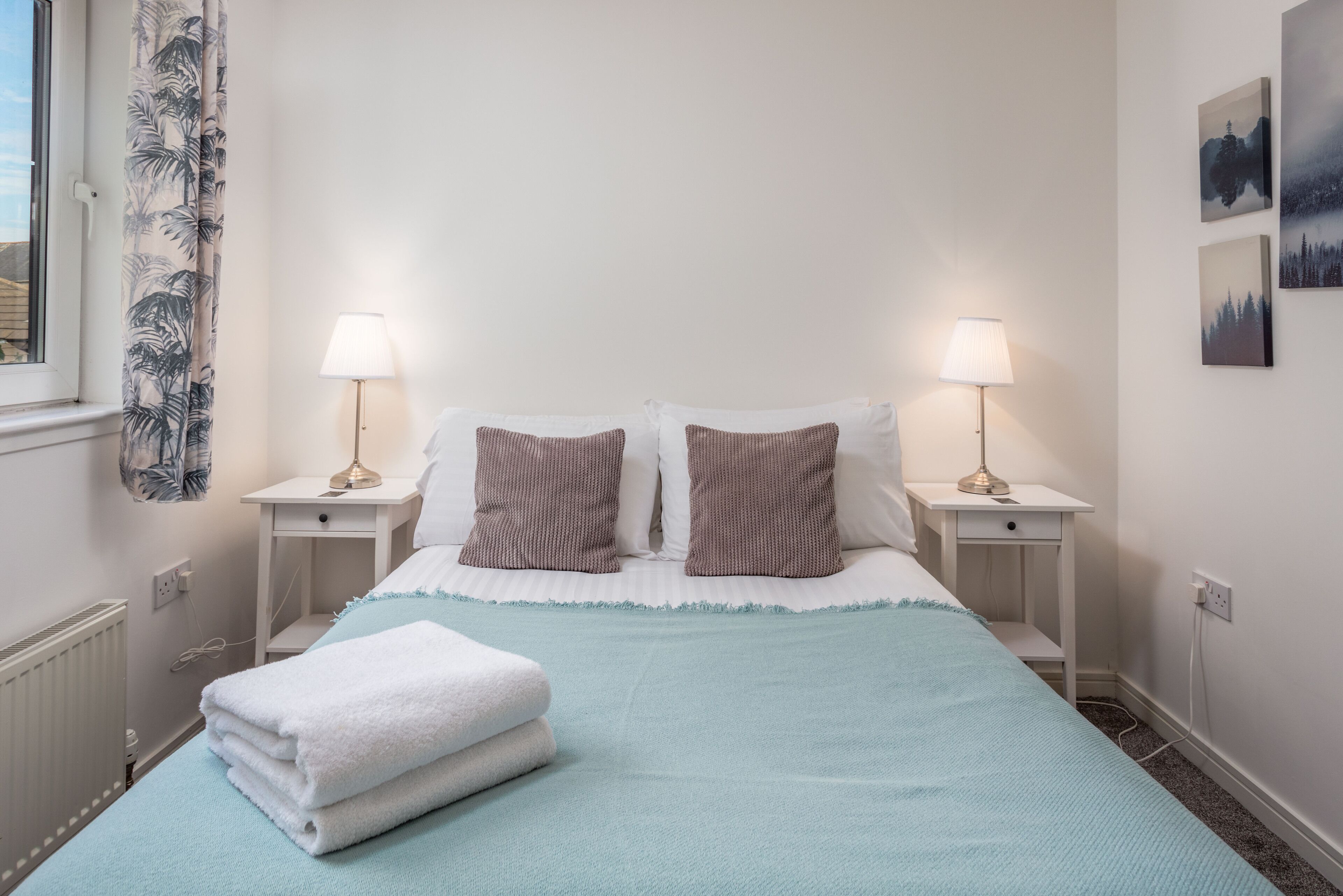 Ein ordentlich bezogenes Bett mit weißen und braunen Kissen, zwei Nachttischlampen und einer blauen Decke.