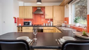 A modern kitchen with wooden cabinets, a black countertop, and a dining area with chairs and a table set for two. - Walker Suite No82 - Donnini Apartments (Kilmarnock)