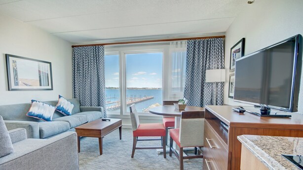 Une chambre d’hôtel équipée d’un canapé, d’une table à manger, de chaises, d’une télévision et offrant une vue sur la mer.
