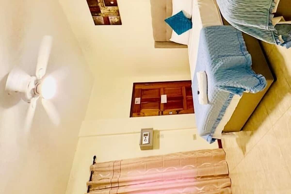 A bedroom with a bed, a ceiling fan, a small wall clock, and a window with curtains.