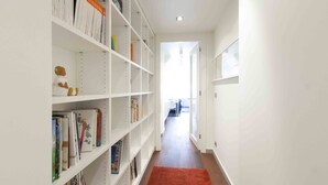 Ein Flur mit weißen Regaleinheiten, gefüllt mit Büchern und Dekoartikeln, der zu einem hellen Raum mit einer weißen Tür führt.