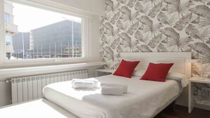 Ein Hotelzimmer mit einem großen Bett, zwei roten Kissen, einem weißen Kopfteil und einem Fenster mit Blick auf Gebäude.