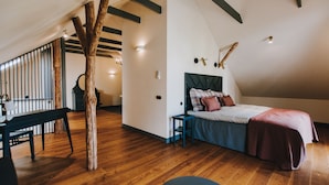 Un dormitorio con piso de madera, una cama con cabecera, un banco y una mesa de comedor.