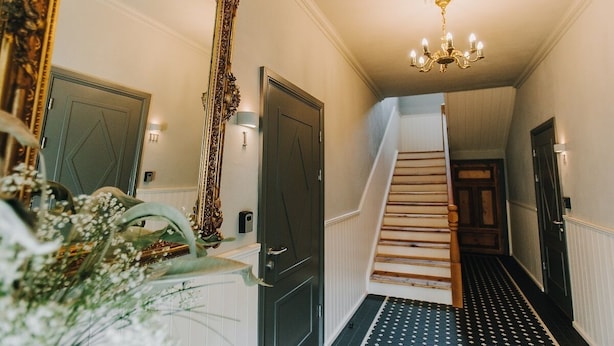 Un pasillo con una escalera, un espejo grande y ornamentado, y un candelabro.