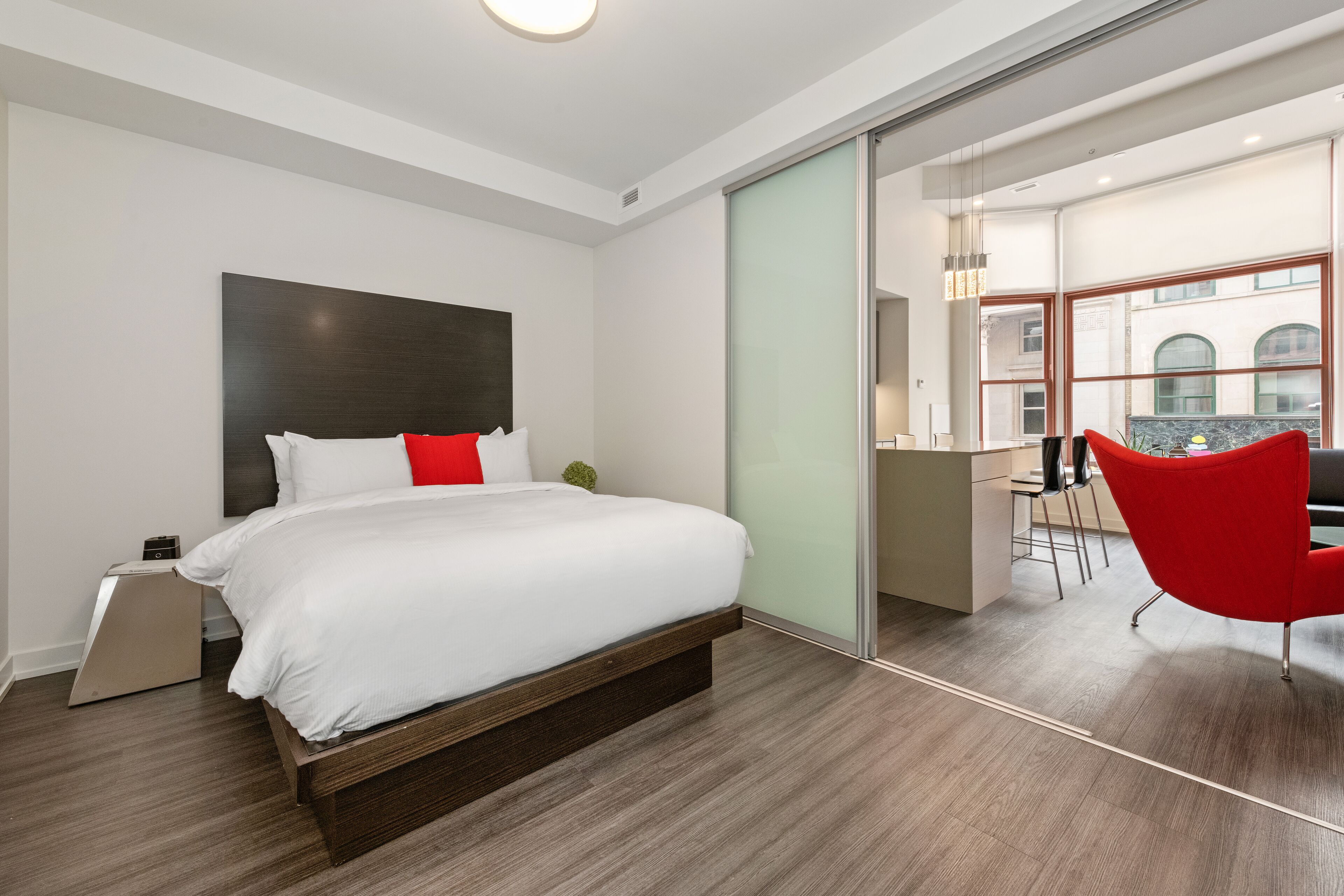 A modern hotel room with a large bed, a desk, and a red chair.