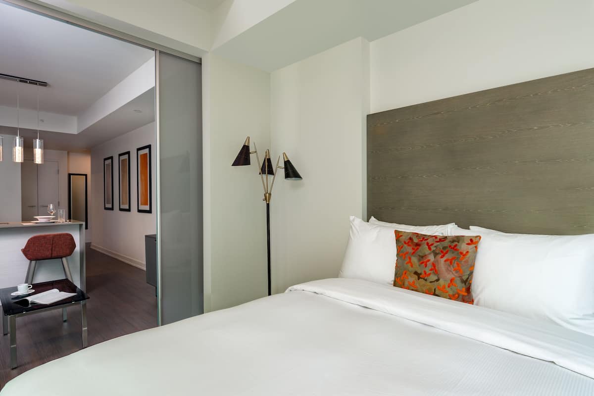 Une chambre d’hôtel moderne avec un grand lit, une table de chevet, une chaise et une lampe sur pied.