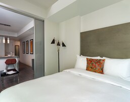 Una habitación de hotel moderna con una cama grande, una mesita de noche, una silla y una lámpara de pie.