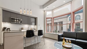 A modern kitchen with a built-in microwave, two black chairs, and a glass coffee table with a bottle and glasses. - reStays Ottawa (Ottawa)
