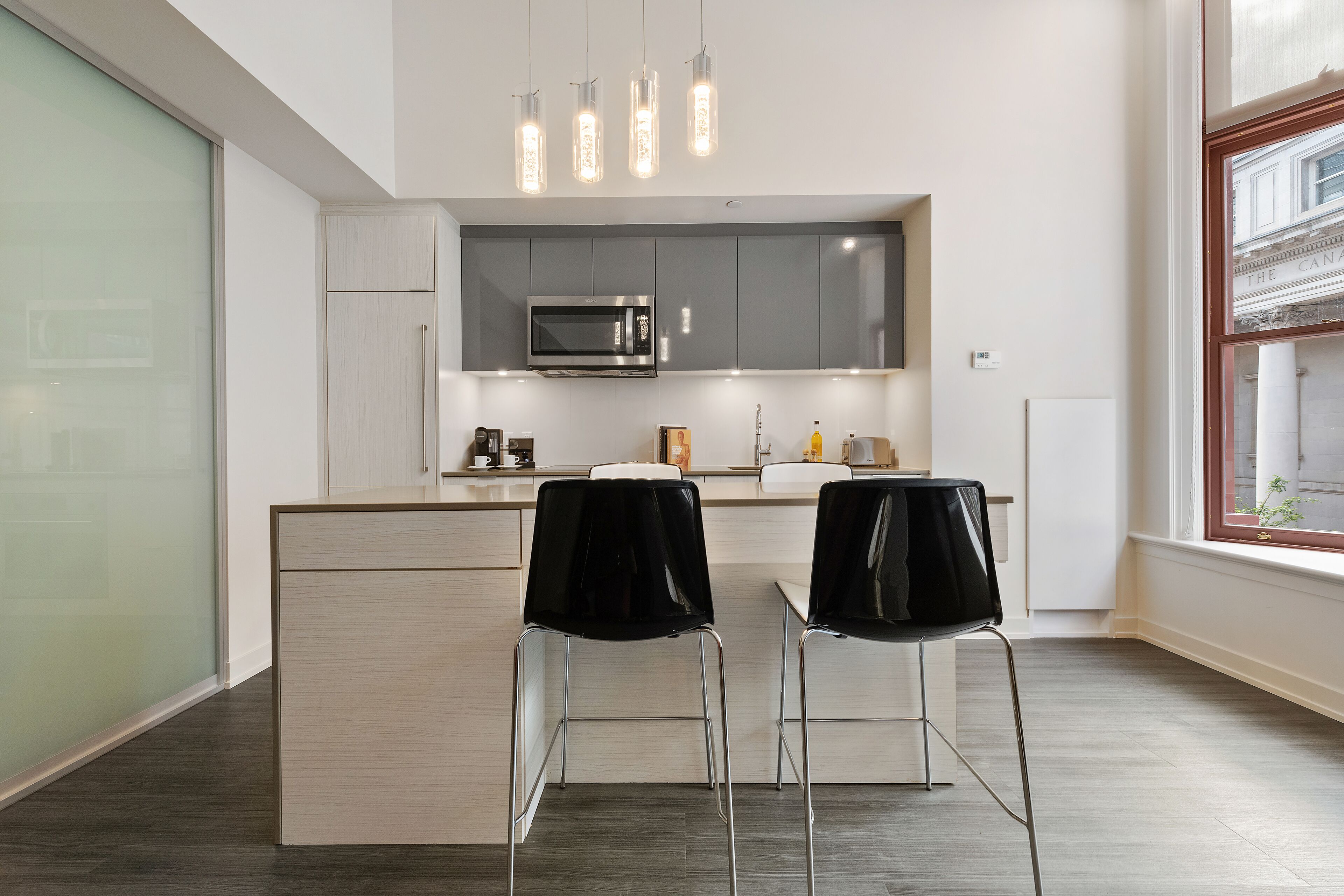 A modern kitchen with a built-in microwave, two bar stools, and pendant lighting.