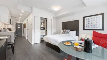 Habitación de hotel moderna con cama, una mesa de vidrio con desayuno, una silla roja y una kitchenette.