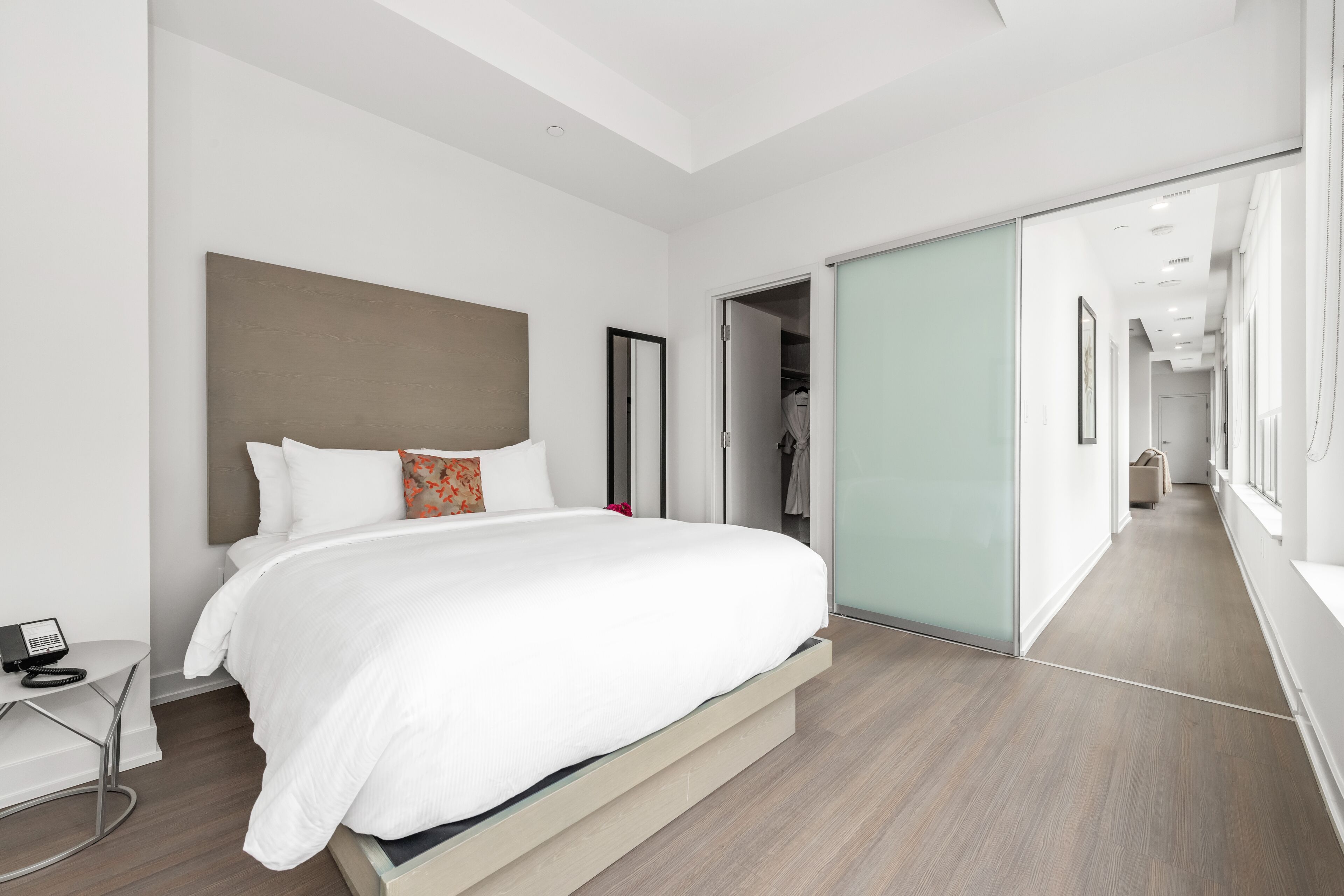 Una habitación de hotel moderna con una cama grande, un teléfono en la mesita de noche y una puerta corredera que da a un pasillo.