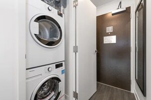 Un cuarto de lavandería con lavadoras y secadoras apiladas, una puerta con un letrero y piso de madera.