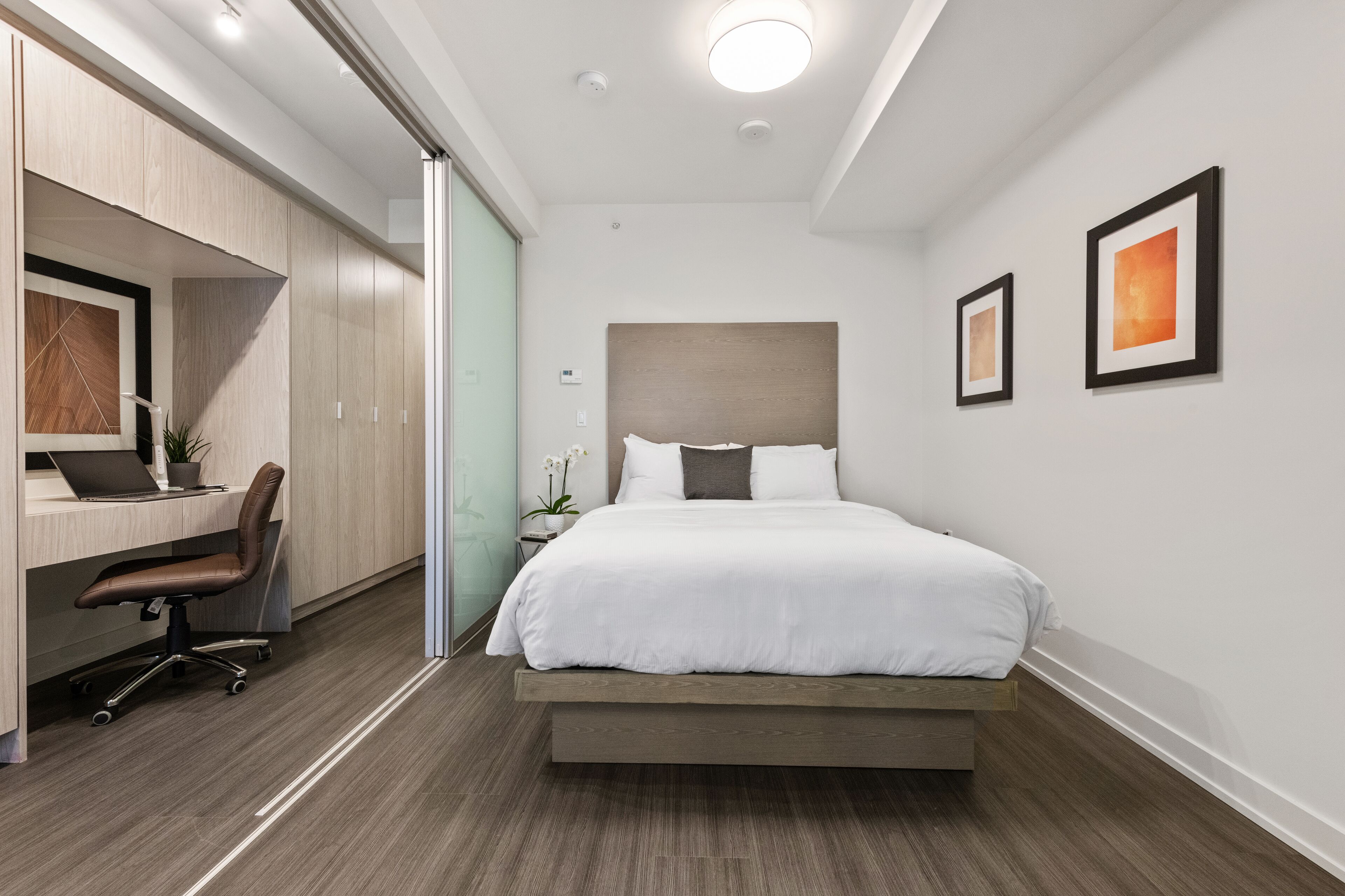 A modern hotel room with a bed, desk, chair, and two framed pictures on the wall.