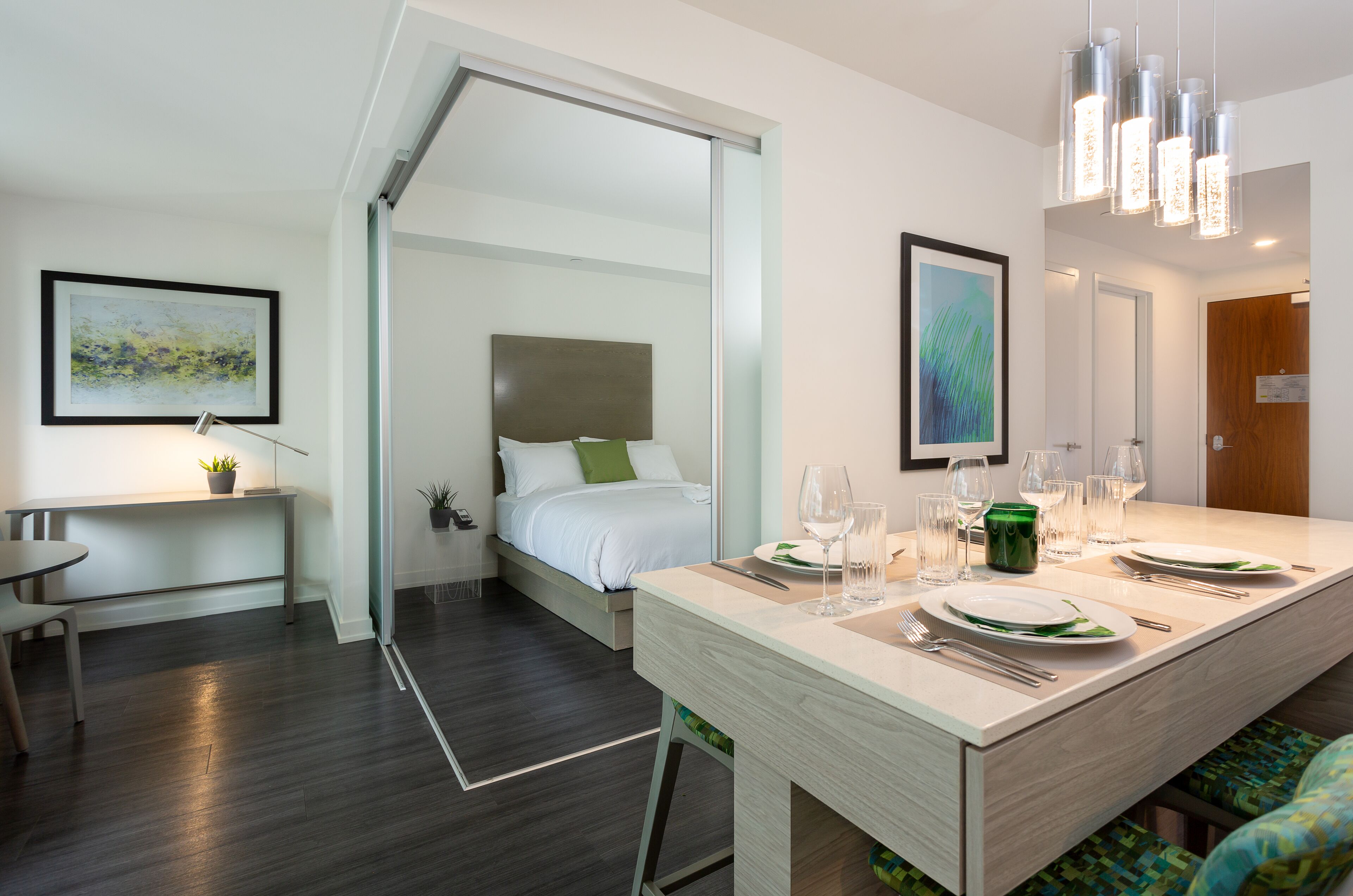 Una habitación de hotel moderna con cama, zona de comedor con mesa puesta para dos personas y un espejo grande.
