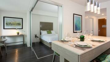 Una habitación de hotel moderna con cama, zona de comedor con mesa puesta para dos personas y un espejo grande.