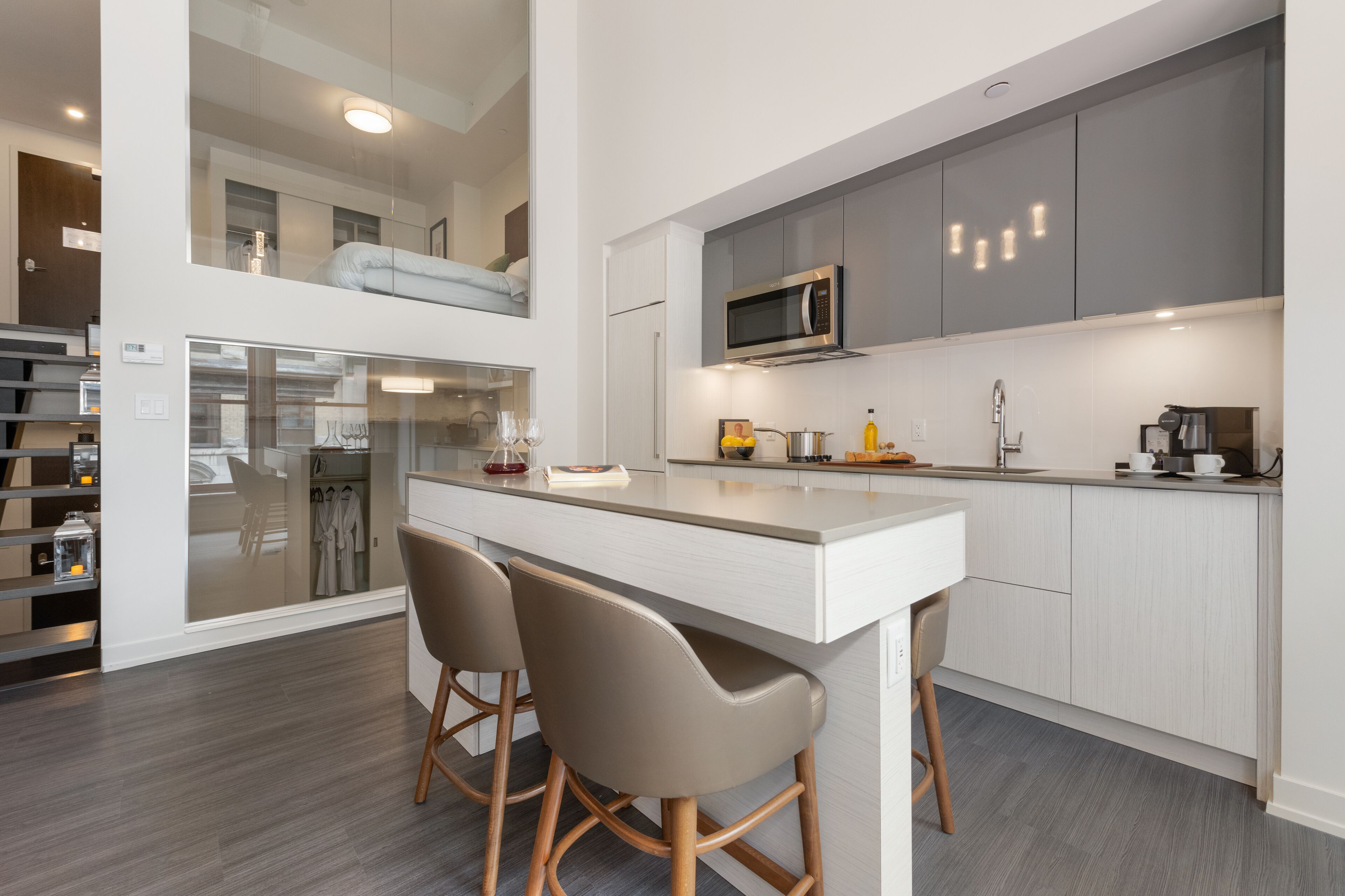 A modern kitchen with a central island, bar stools, and a microwave.