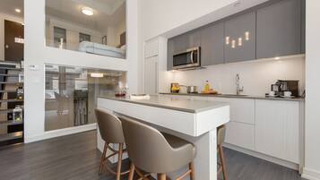 A modern kitchen with a central island, bar stools, and a microwave.