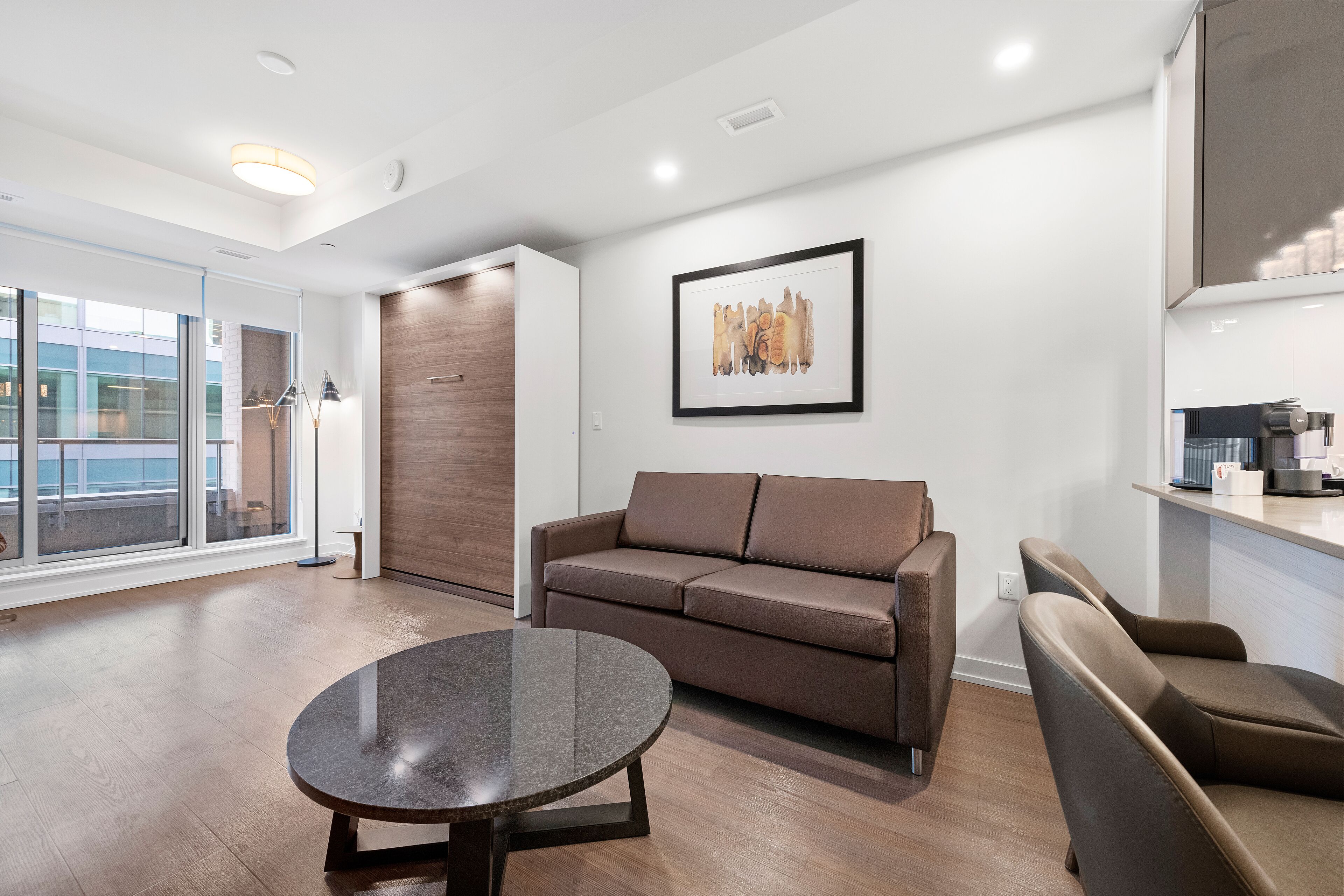 A modern living room with a brown leather sofa, a round coffee table, and a framed artwork on the wall.