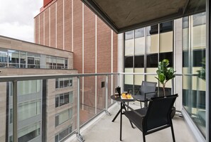 Un balcon avec une table et des chaises, un pot de fleurs et une vue sur un immeuble en briques.