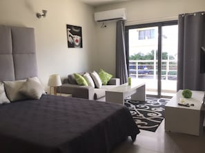 Ein modernes Hotelzimmer mit einem großen Bett, einer Sitzecke, einem kleinen Tisch und einem Balkon mit Blick.
