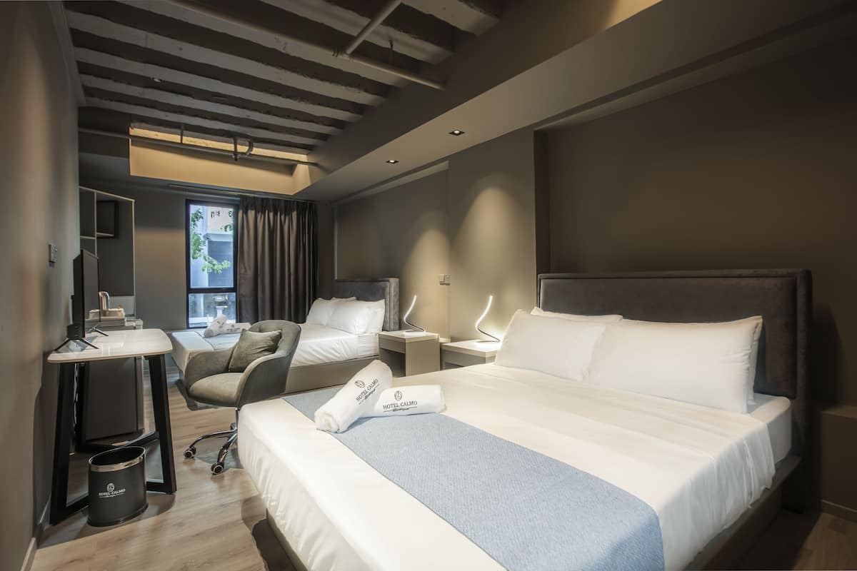 A modern hotel room with a large bed, a desk, a chair, and a small table.