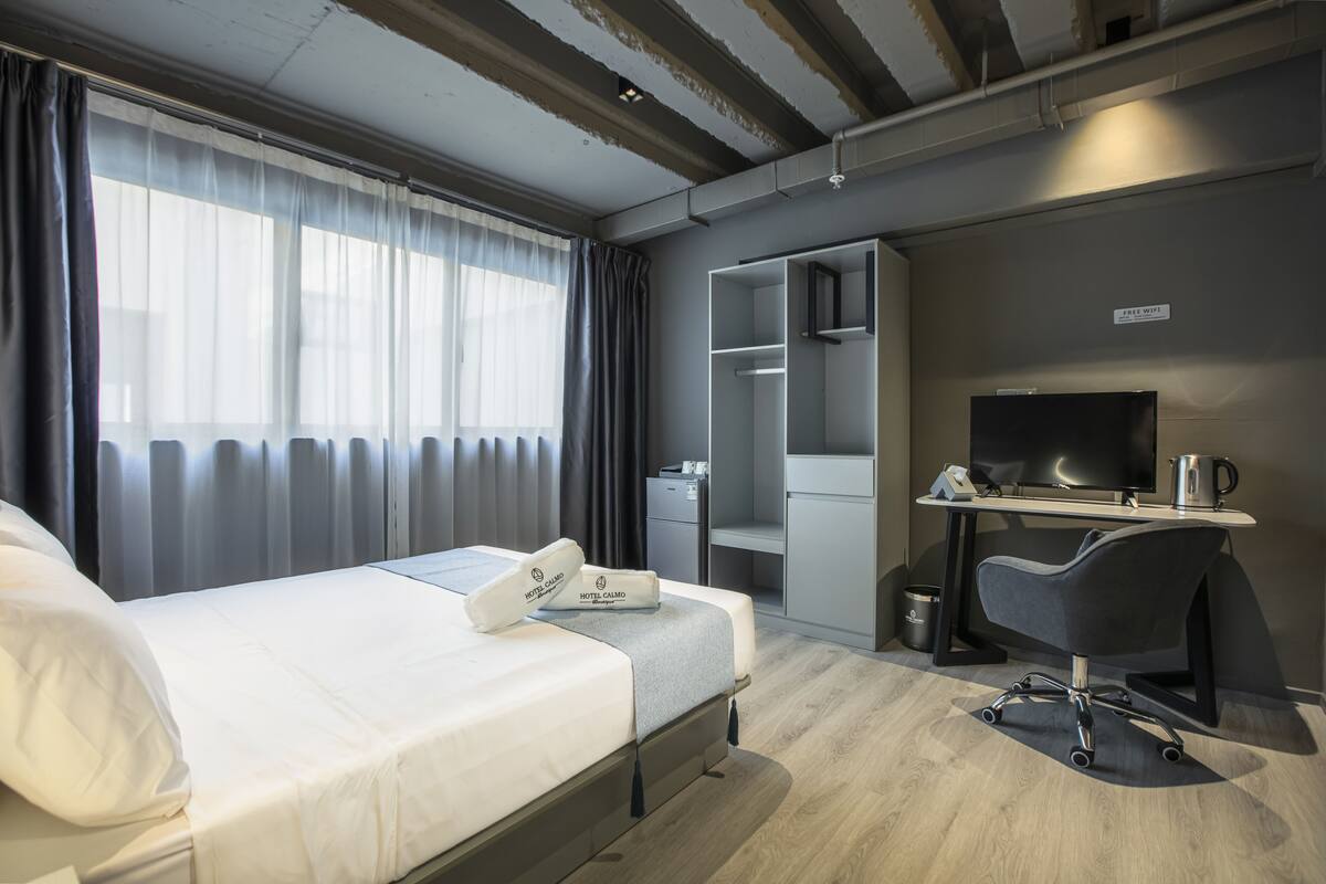 A hotel room with a bed, a desk, a chair, a television, and a minibar.