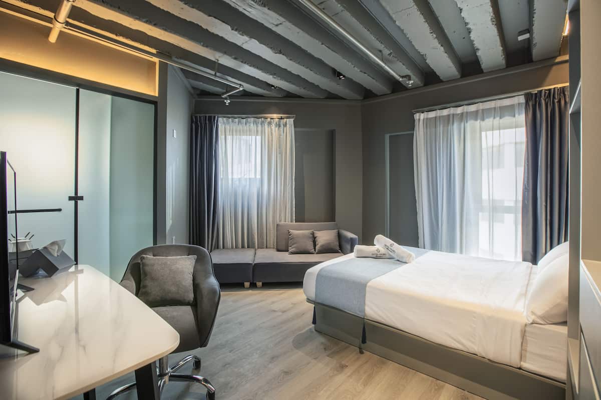 A modern hotel room with a bed, sofa, desk, and chair.