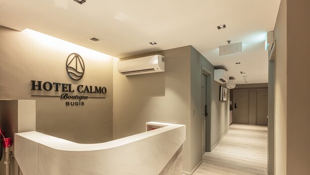 Zona de recepción de un hotel con un mostrador de mármol, equipo de aire acondicionado montado en la pared y un pasillo que conduce a las habitaciones de huéspedes.