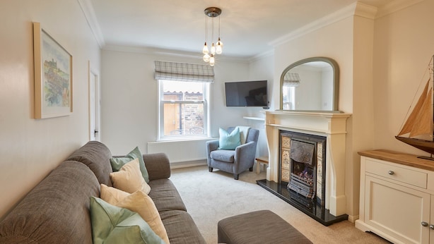 A living room with a brown sofa, a fireplace, a television, and a window with a view of the outside. - Adventure House (Whitby)